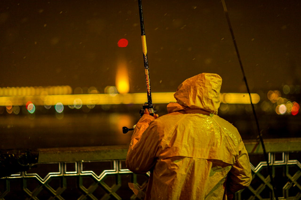 A fisherman in a yellow raincoat fishes on a rainy night on Galata Bridge, Istanbul.