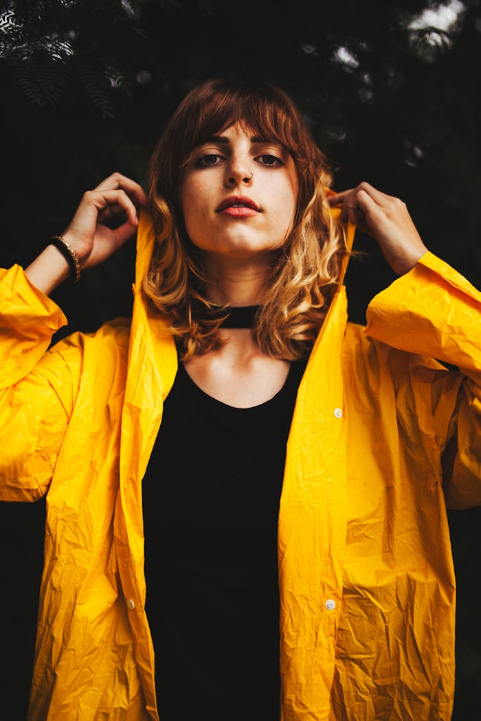 Portrait of a young woman wearing a black dress and a yellow raincoat outdoors, showcasing style and confidence.